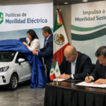 Autoridades de movilidad electrica firman un convenio en un evento oficial con un automovil electrico blanco y banderas mexicanas