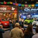 Feria automotriz con stands de Autos TT y Olinia, con visitantes observando vehículos eléctricos